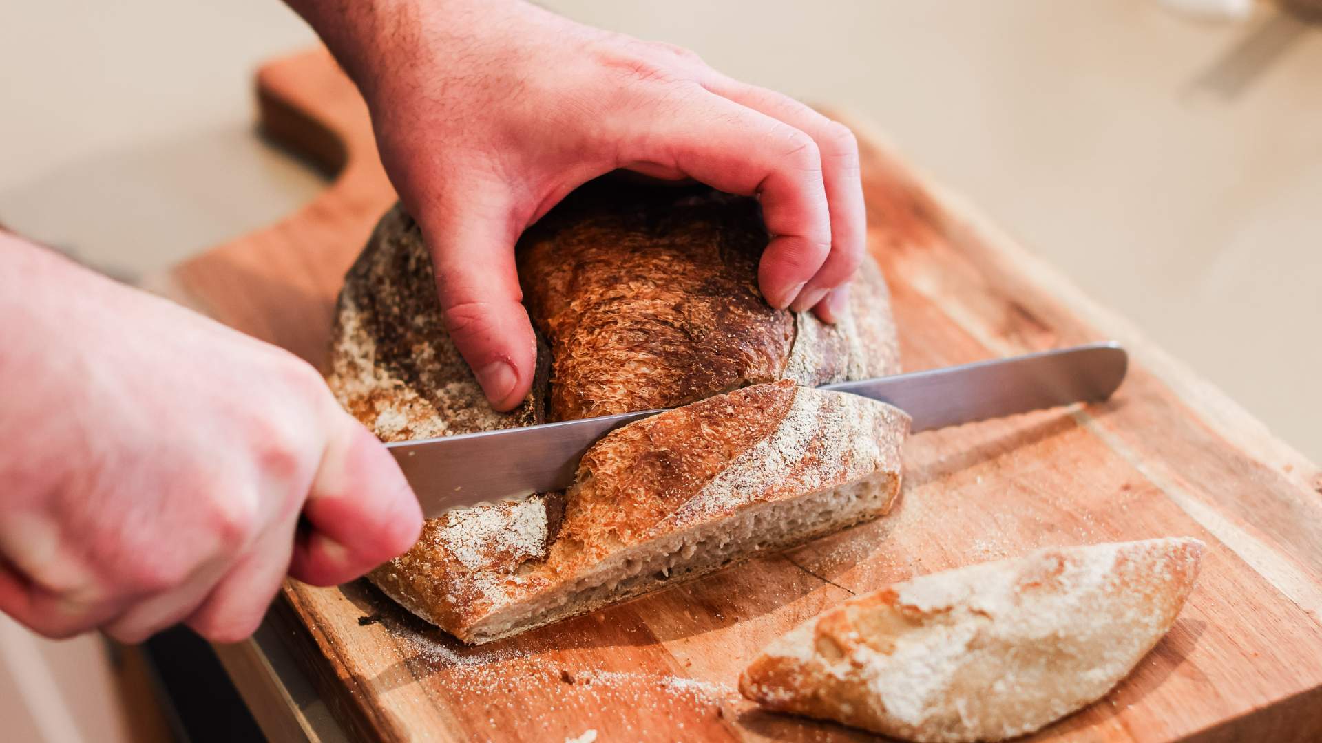 Hands slicing a fresh sourdough loaf